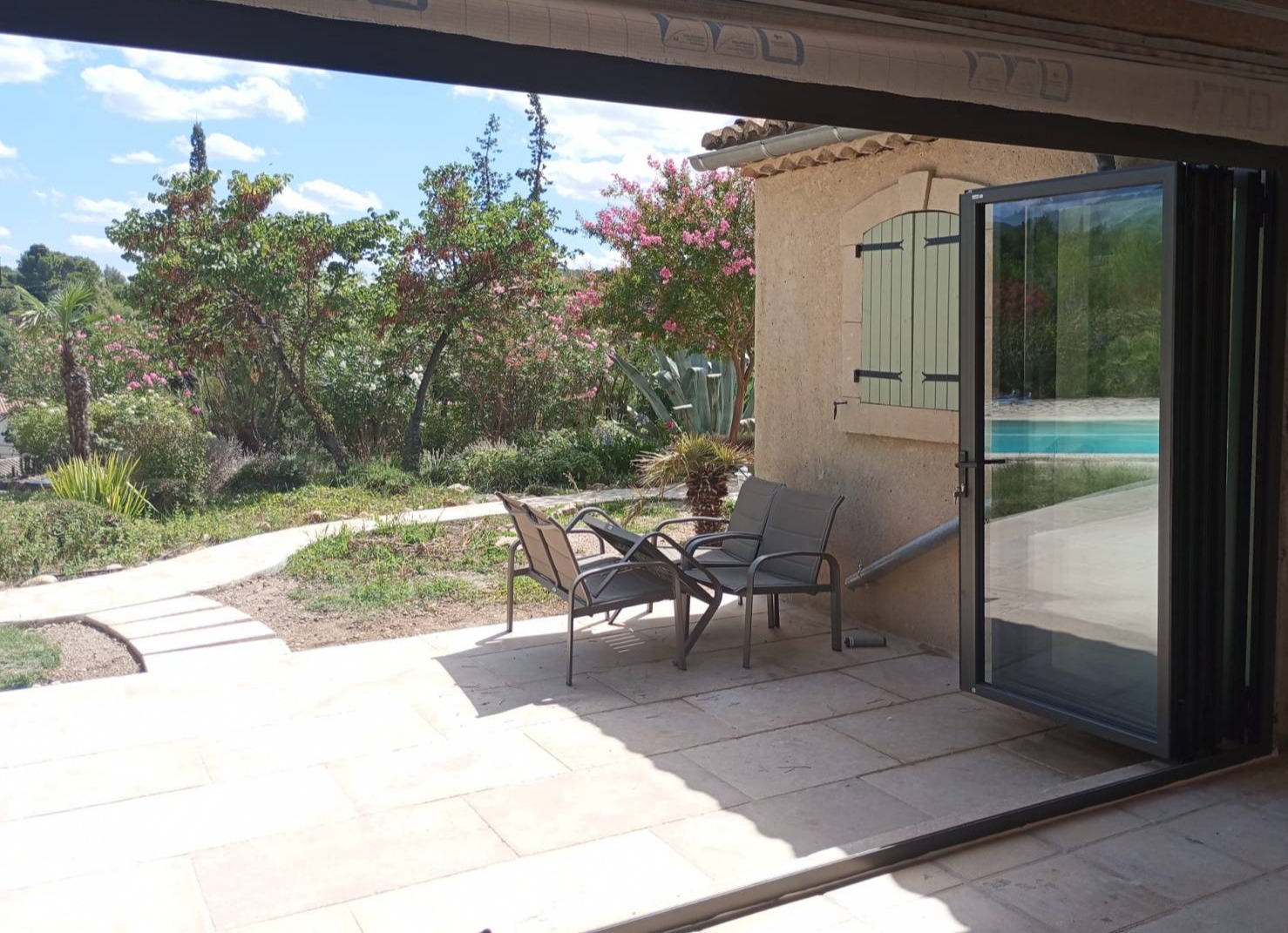 Mise en place d’une baie vitrée coulissante accordéon sur mesure en aluminium sur Mirabel aux Baronnies, avec porte de service intégrée et ouverture extérieure